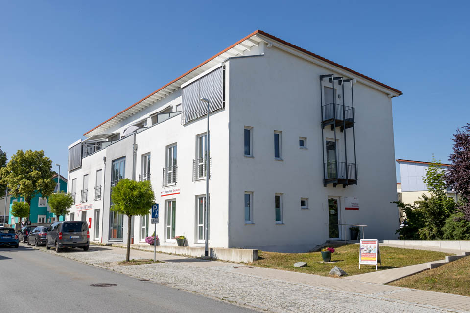 Außenansicht der BRK-Tagespflege in Gangkofen von der Hauptstraße aus. Die Tagespflege ist in einem 3-stöckigen, weißen Gebäude untergebracht.
