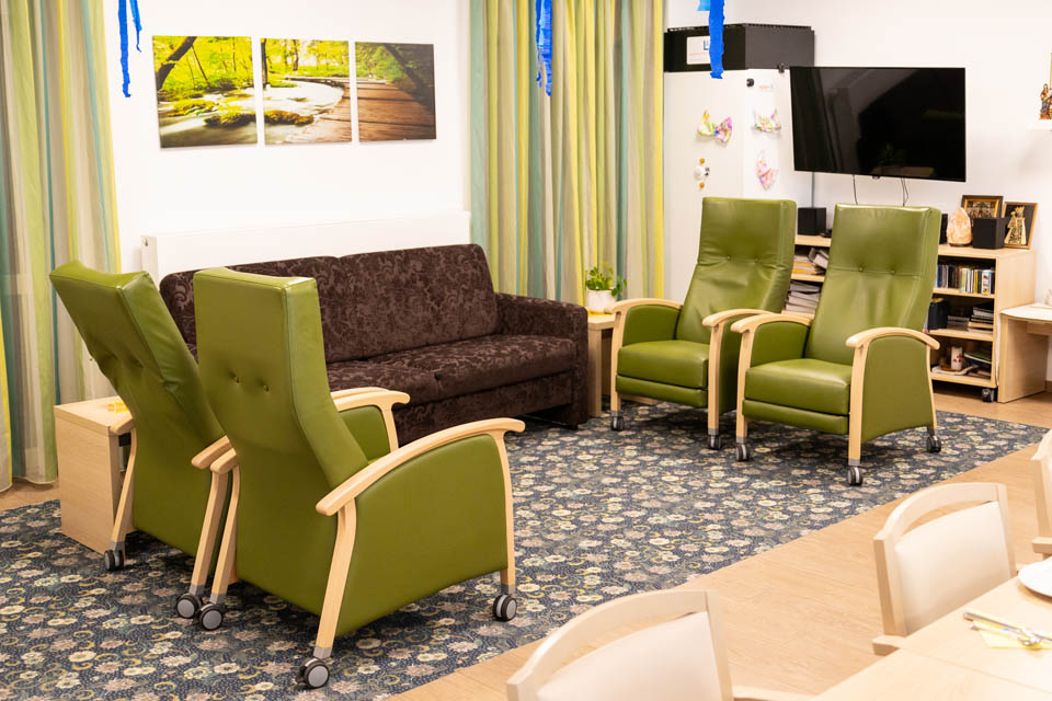 Der Stuhlkreis in der BRK-Tagespflege Gangkofen ist Hufeisenförmig angeordnet. Am Kopfende steht eine braune Couch, seitlich flankierend sind jeweils 2 grüne Sessel aufgetstellt.
