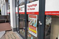 Eingangsbereich der BRK-Tagespflege St. Florian in Eggenfelden. Die Türen und Fenster sind im weiß-roten Design des Roten Kreuzes beklebt. Auf der Tür steht in roten Buchstaben Tagespflege St. Florian. Darunter hängt ein Plakat mit dem Titel "hereinspaziert", welches zum kostenlosen Schnuppertag einlädt.